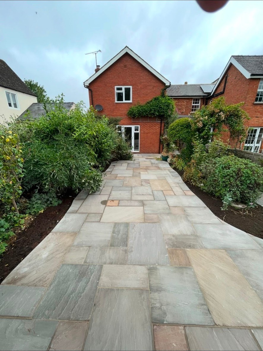 Natural riven stone patio path leading to a red brick house with borders and shrubs.