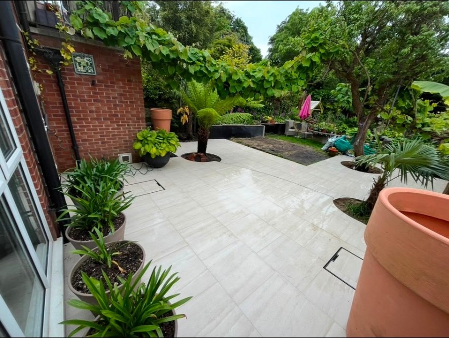 Modern light grey porcelain patio with circular tree cut-outs and potted garden plants.