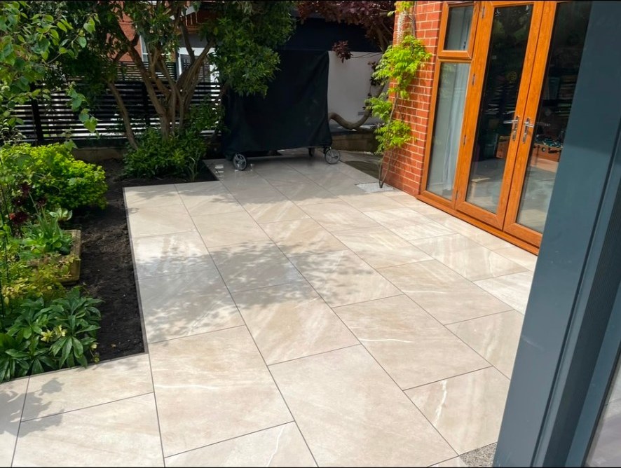 Contemporary beige porcelain tiled patio leading to timber bifold doors and garden borders
