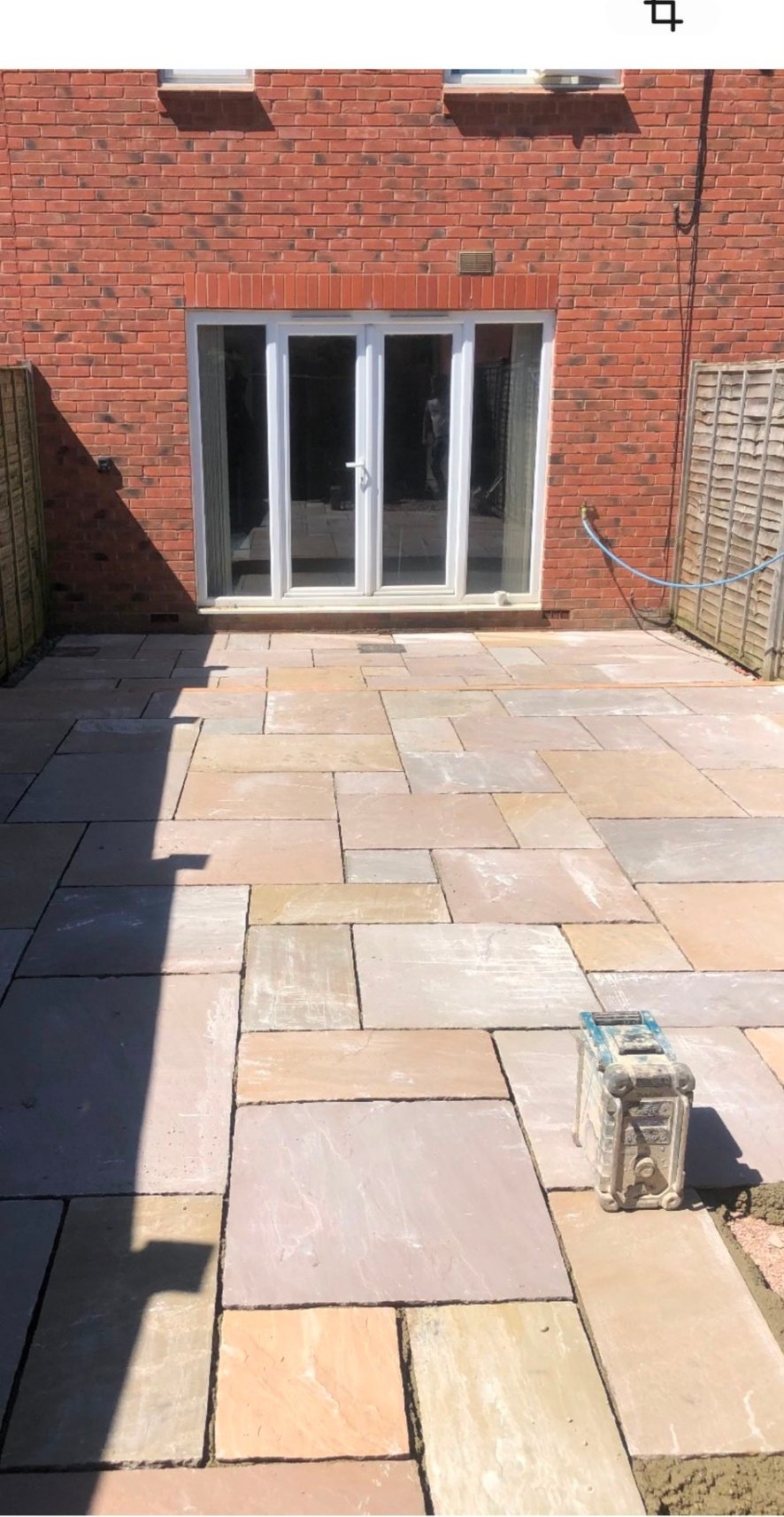 Riven natural stone patio flags being laid in a garden with multi-tonal sandstone paving.
