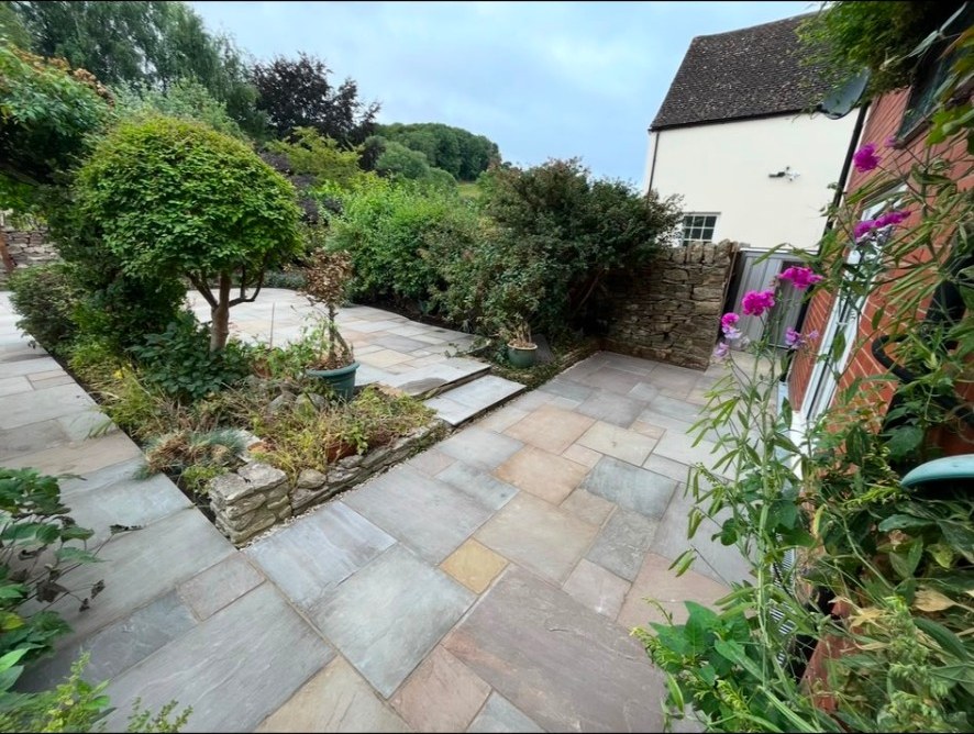 Tiered natural stone patio with riven sandstone flags, stone walling and garden planting.