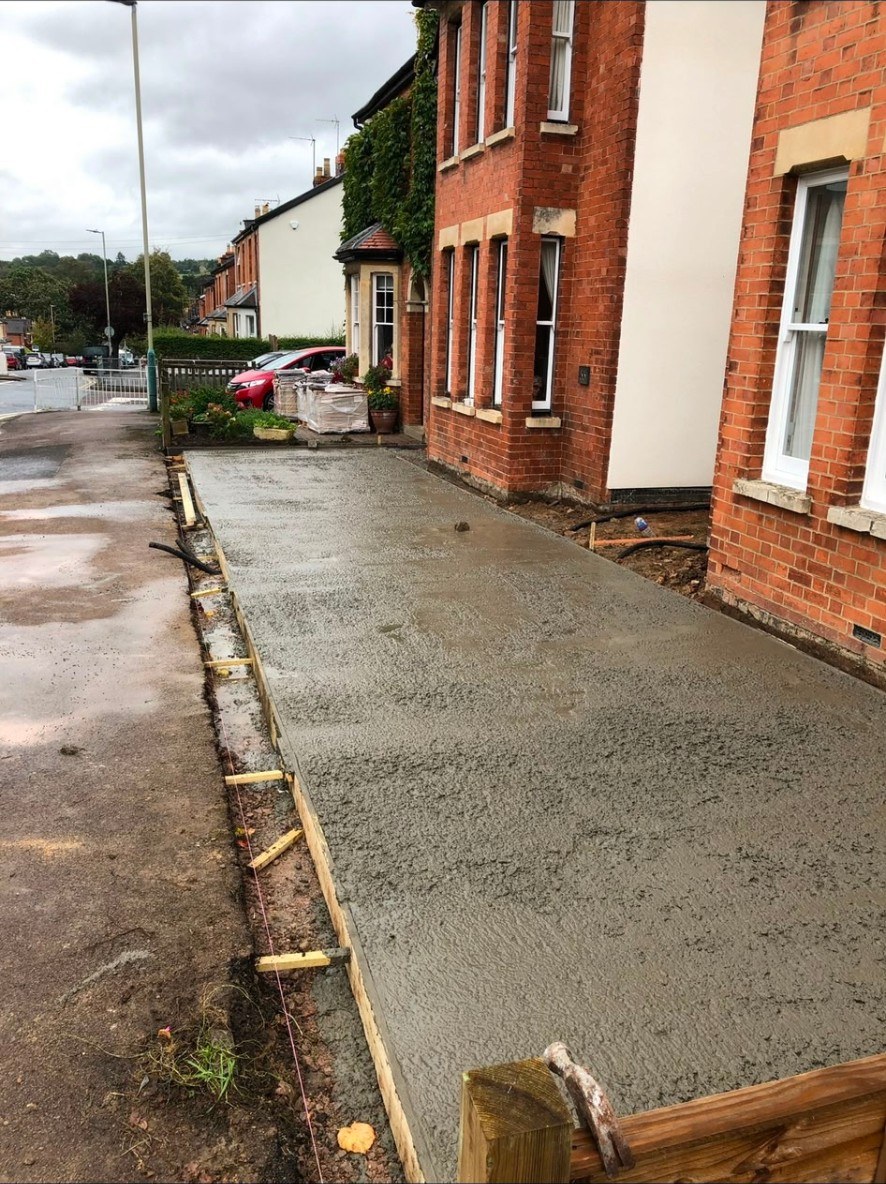 Freshly poured concrete sub-base for a new driveway alongside a Victorian red brick house.