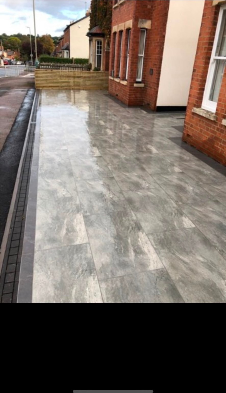 Contemporary grey marble-effect porcelain paving beside a red brick house with drainage channel.