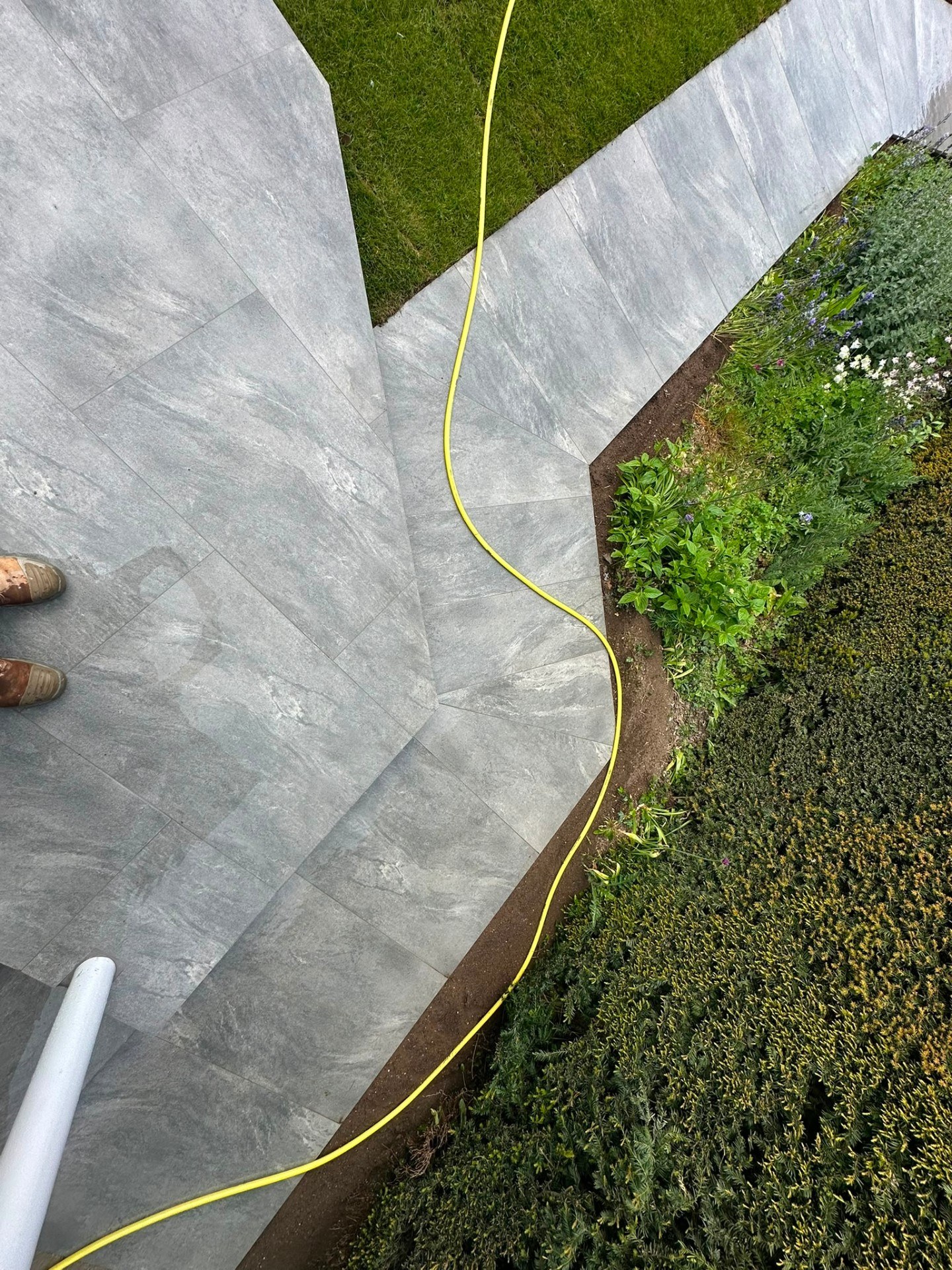 Contemporary grey porcelain paving tiles laid in a garden with mitred corners and curved borders.