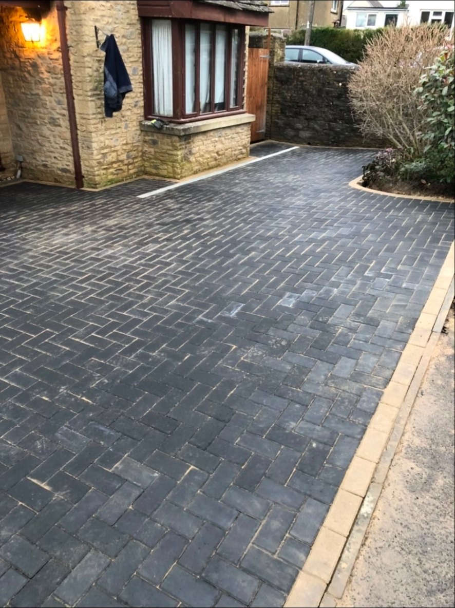 Charcoal herringbone block paving driveway with light-coloured border in front of a stone cottage.
