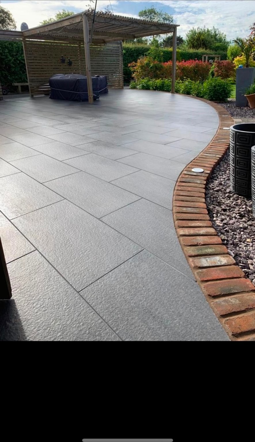 Contemporary grey porcelain patio with a curved brick edge and timber pergola