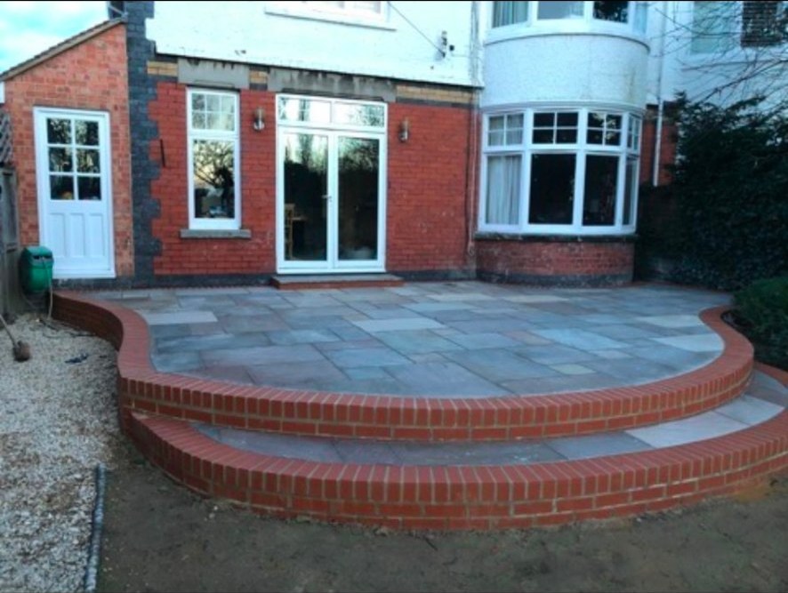 Sandstone patio with curved red brick steps and border.