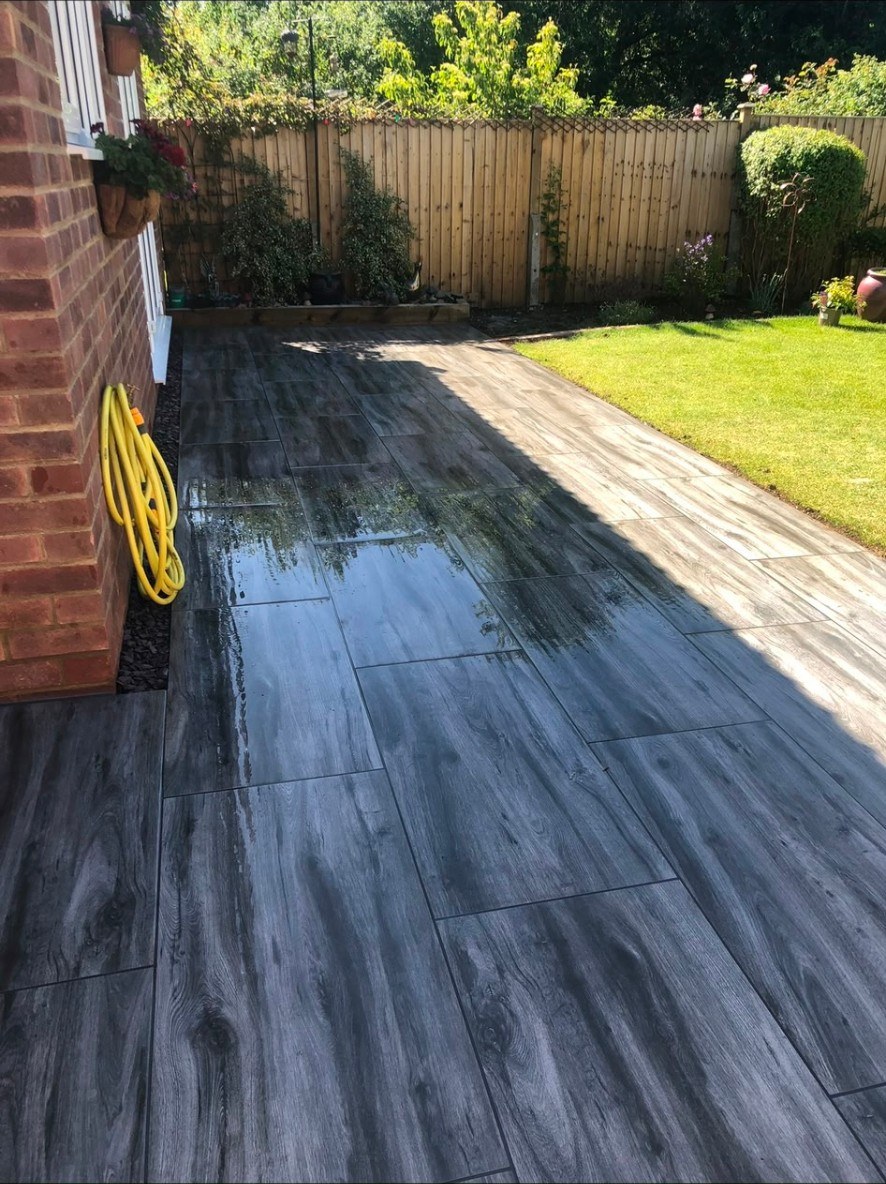 Contemporary grey wood-effect porcelain paving patio next to a garden lawn.