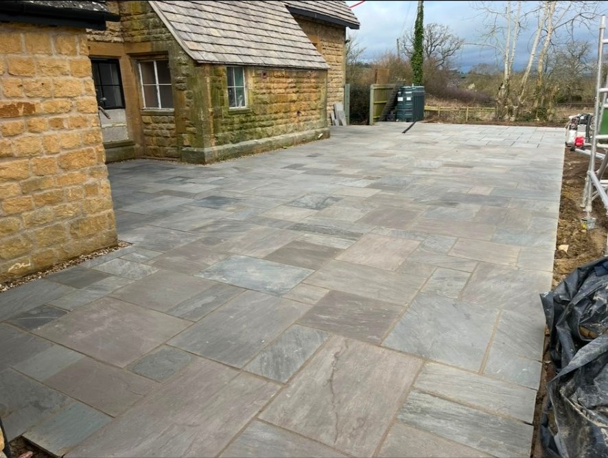 Newly laid natural stone patio flags in a multi-size pattern alongside a stone cottage.