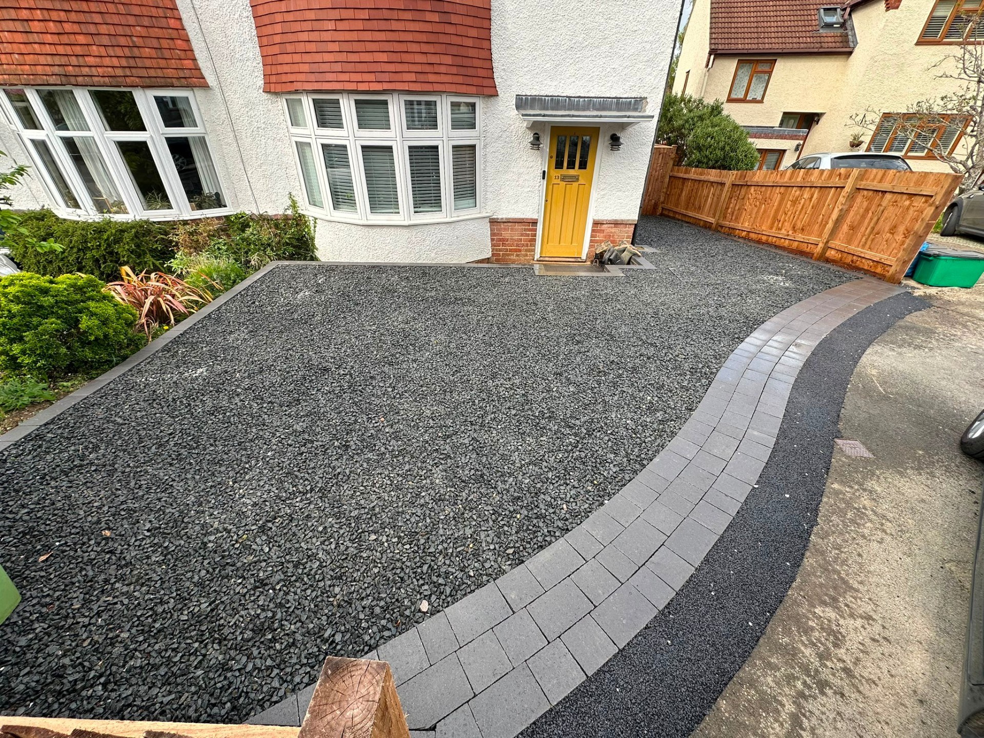 Shingle driveway with curved grey block paving border and timber panel fencing.