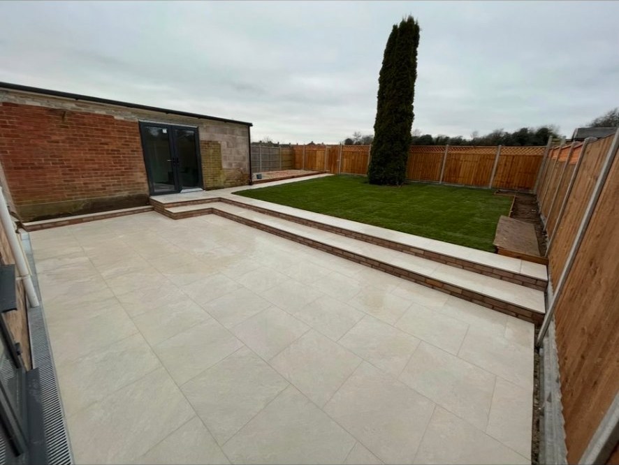 Modern garden with porcelain patio, tiered steps, freshly laid lawn and timber fencing.