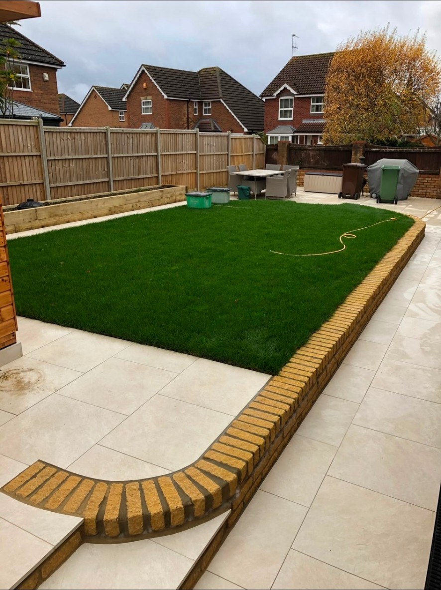 Modern tiered garden with porcelain paving, brick wall, fresh lawn, and timber fencing.