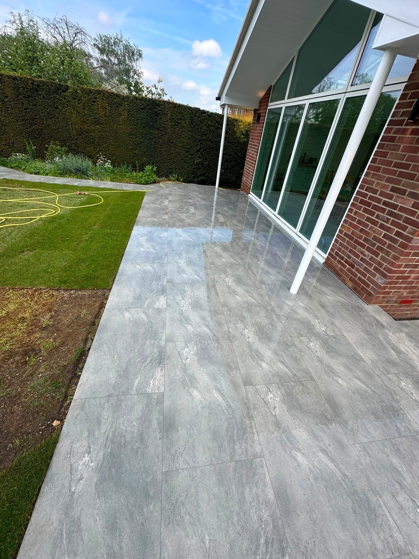 Modern grey porcelain patio paving alongside a fresh lawn and house extension.