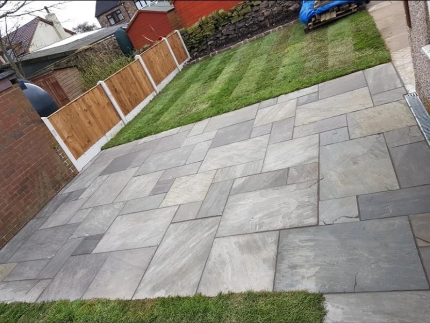 Riven natural stone patio with grey sandstone flags next to a freshly striped lawn.