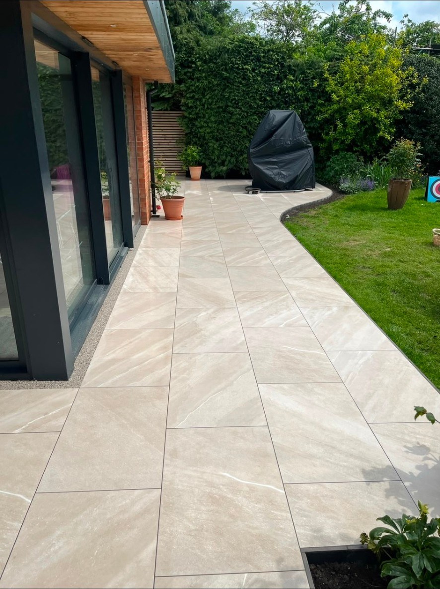 Contemporary beige porcelain tiled patio and curved garden path next to a lawn and modern home